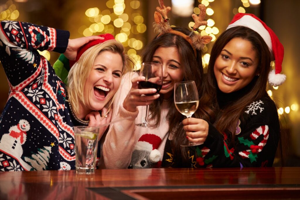 Friends in holiday sweaters drinking wine at a party.